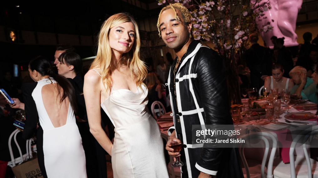 Women in a white dress, man in a leather trench coat jacket at a party
