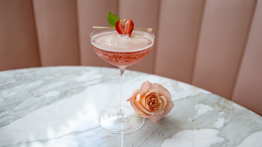 Aphrodise French 75 garnished with a Strawberry next to a pink rose