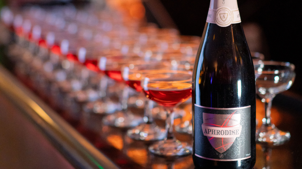 A bottle of Aphrodise in front of a row of coupè glasses filled with Aphrodise Rosé