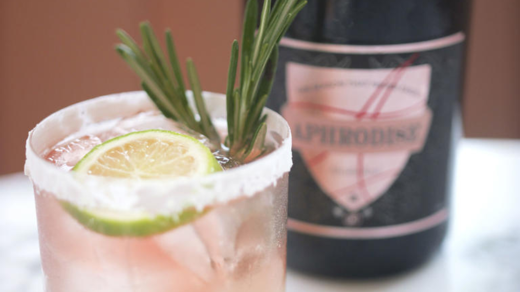 Aphrodise Rosemary Fizz cocktail in front of a bottle of Aprhodise