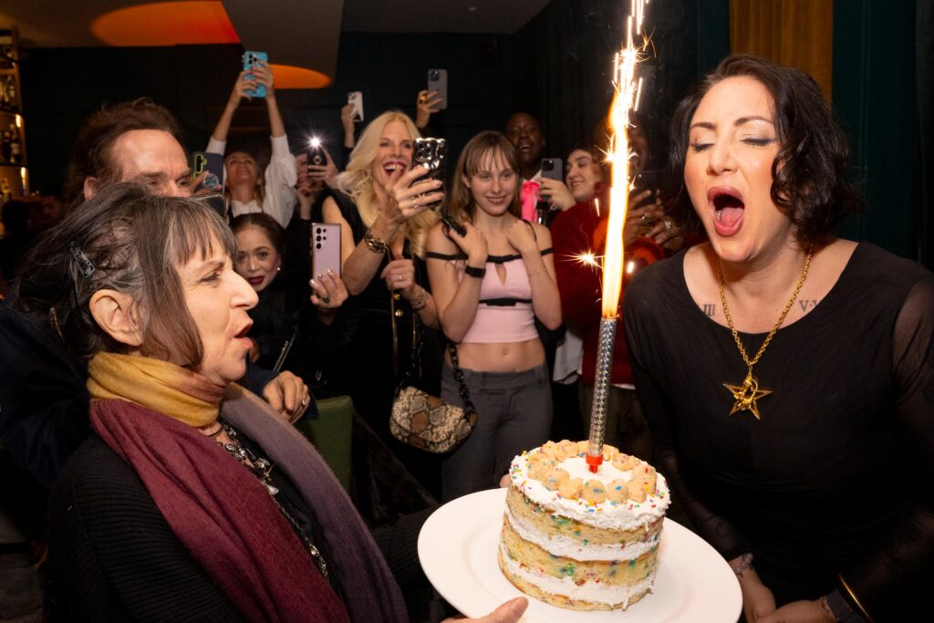 Guests celebrating, watching Nadja Sayej blow out a sparkler candle on her cake