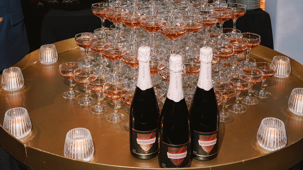 Drink aphrodise bottles lined up with a pyramid of wine glasses behind filled with Aphrodise