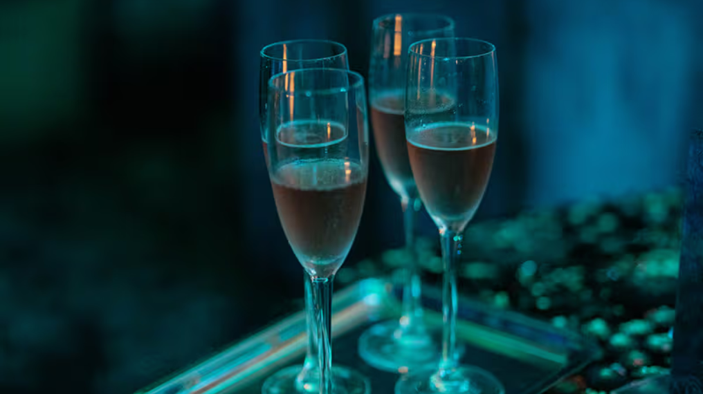 Four flute glasses on a tray in a dark blue lit room